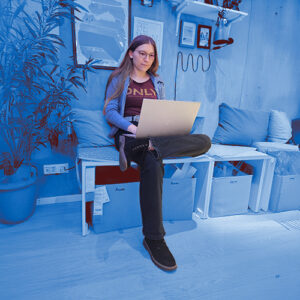 Blau bearbeitetes Bild von mir, auf dem ich am Laptop am Schoß an Design arbeite